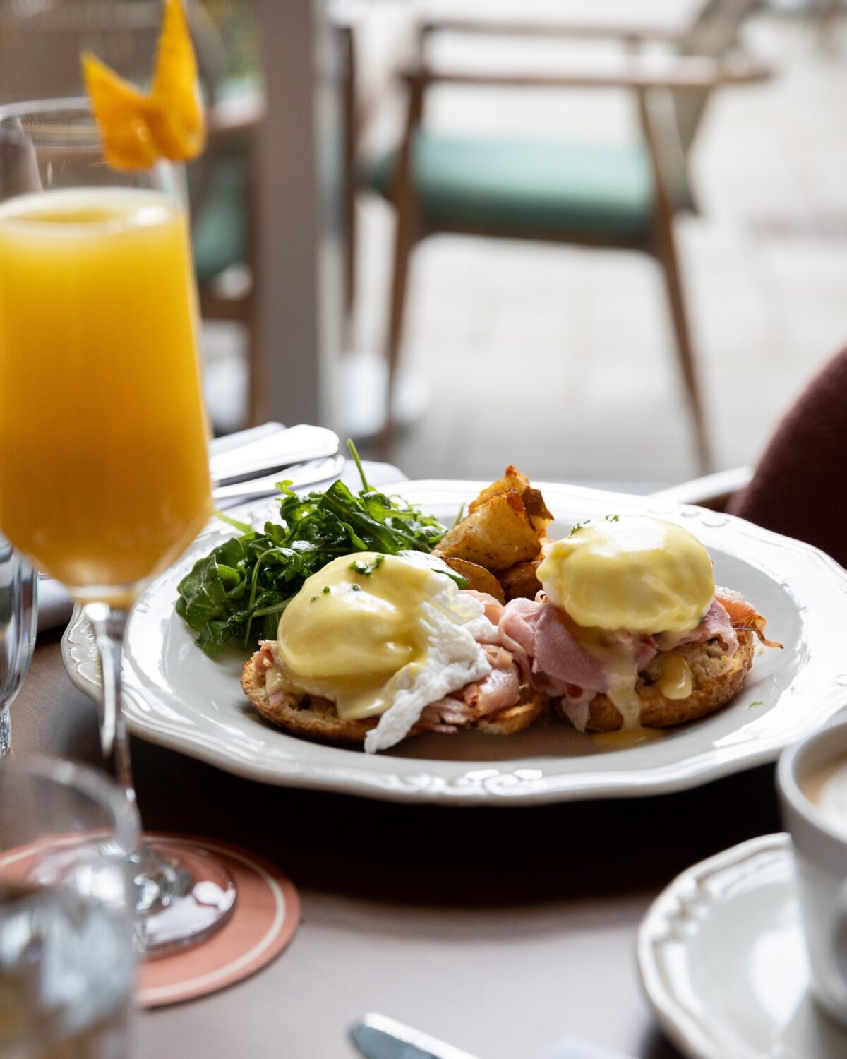 Eggs Benedict with ham, greens, and mimosa on a bright brunch table setting