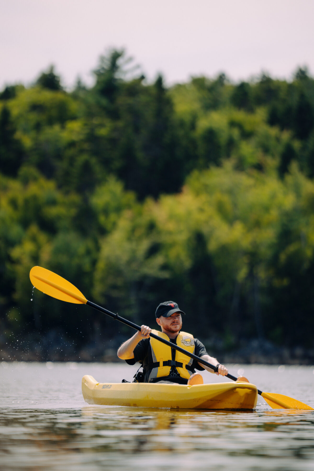 Person kayaking on Long Lake in Halifax, Nova Scotia, paddling across calm water with forested shoreline in the background