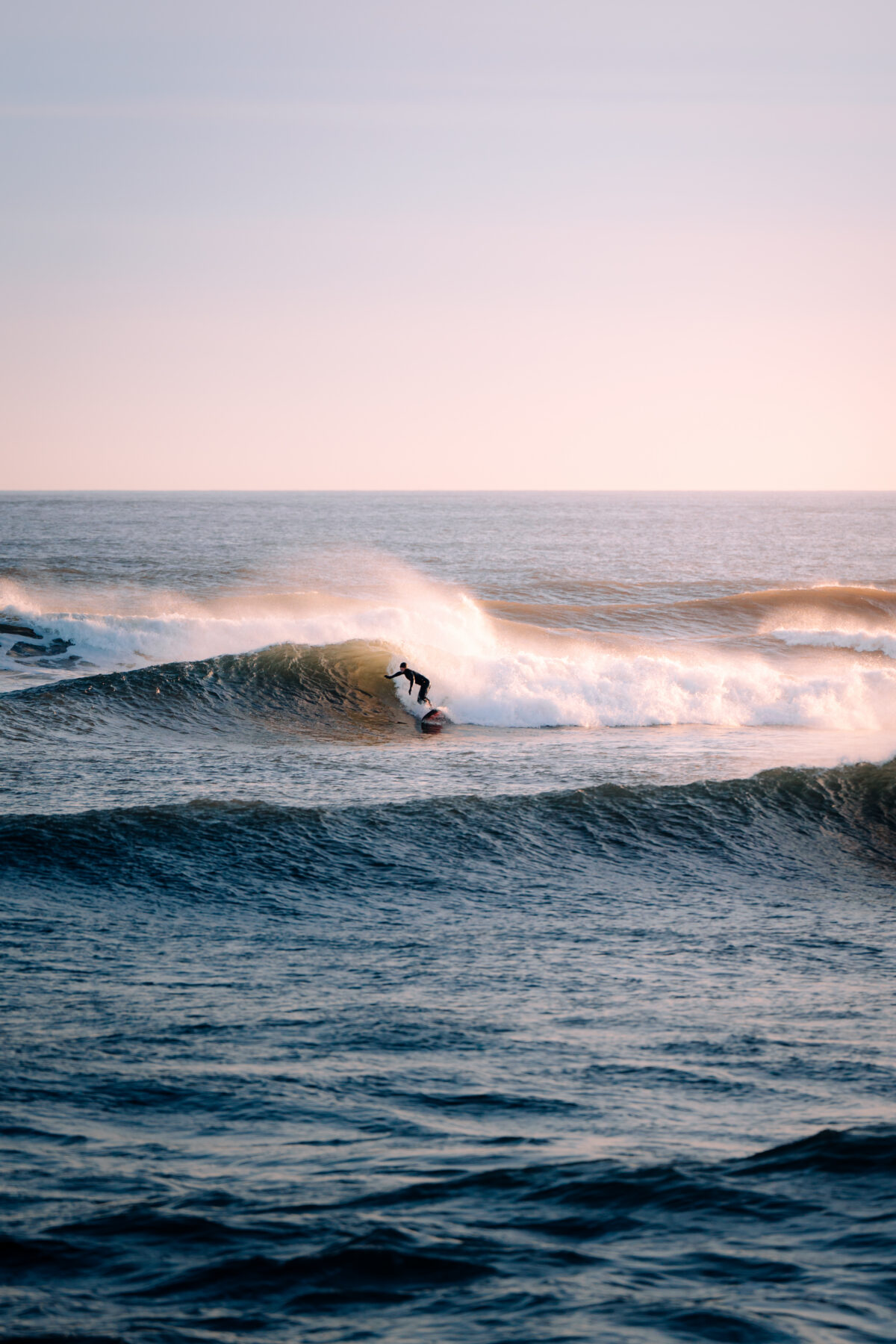 Surfer riding a breaking wave at Lawrencetown Beach near Halifax, Nova Scotia, with glowing sunset light over the Atlantic Ocean