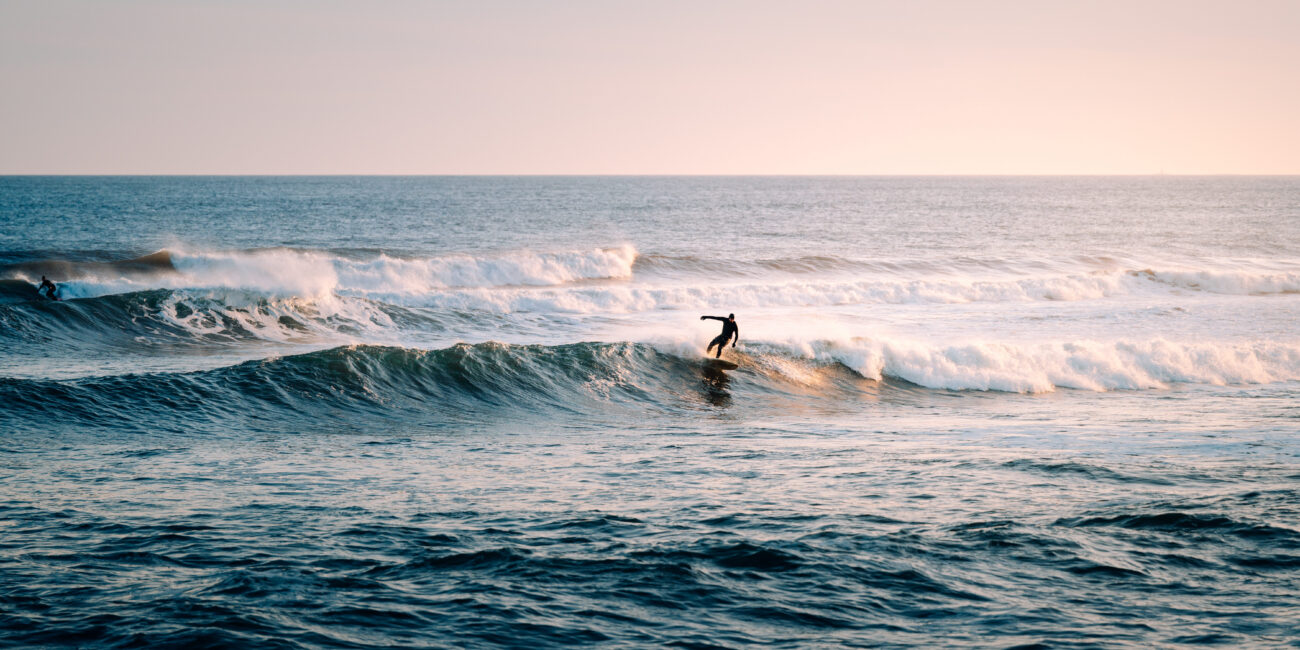 Surfer riding a wave at Lawrencetown Beach near Halifax, Nova Scotia during golden hour, with rolling Atlantic swells in the background