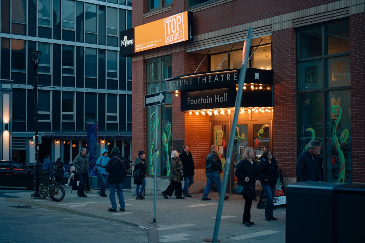 People walking outside Neptune Theatre in Downtown Halifax, with the Fountain Hall entrance lit up beneath the theatre marquee.