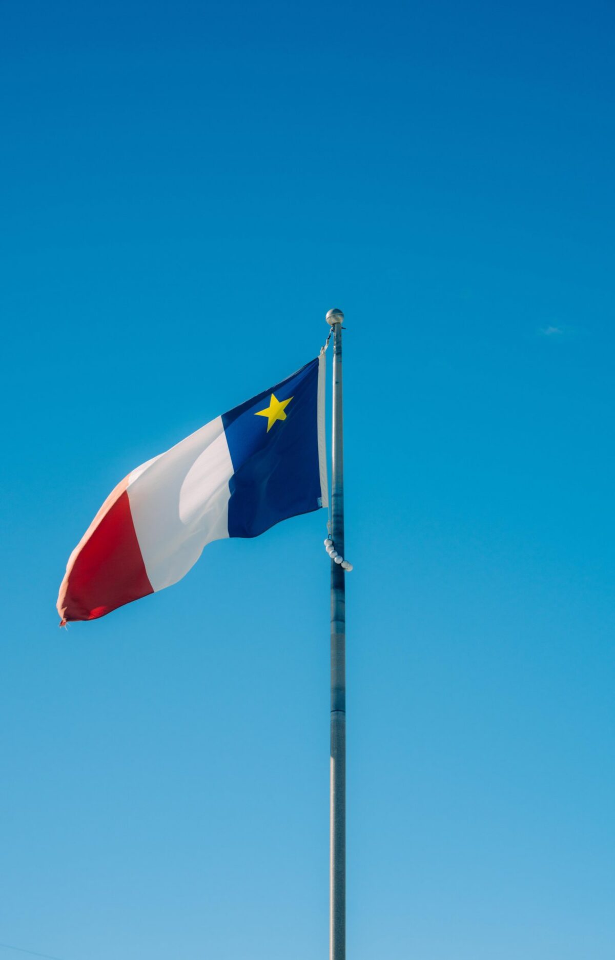Acadian flag flying against a blue sky.
