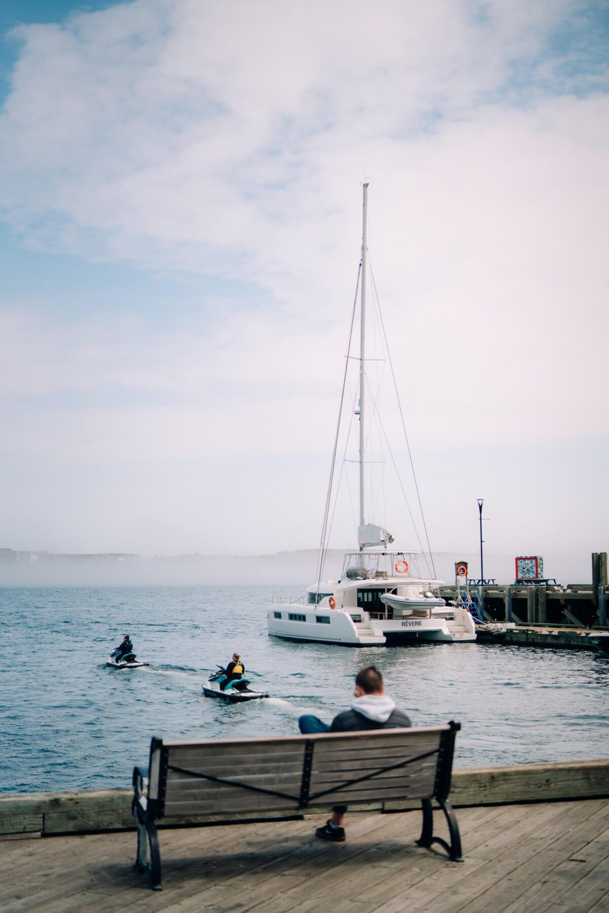Person sitting on a bench at the Halifax Waterfront, watching jet skiiers with a yacht next to them.